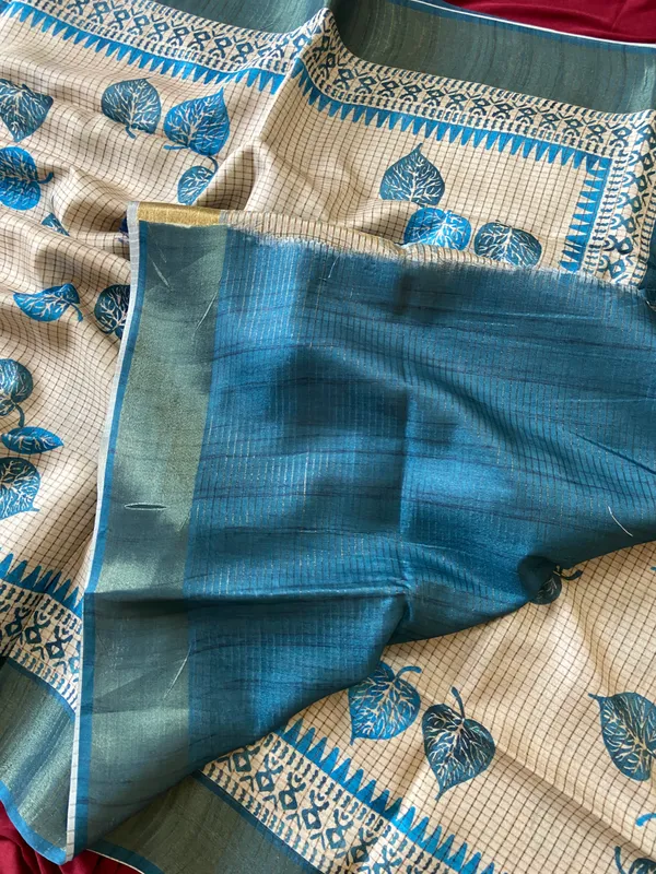 Soft_Tussar_Silk_sarees_with_Beautiful_Hand-Block_Inspired_Leaf_Digitel_Print:_The_primary_motif_consists_of_pipal_leaf_patterns_in_vibrant_shades_With_Temple_Border_The_serrated,_triangular_pattern_lining_the_is_a_classic_Indian_design_known_as_a_Temple_border_or_Temple_motif._This_is_a_staple_in_traditional_South_Indian_textiles_With_Attractive_Checks_Design_Saree_And_Digital_Print_Blouse_With_Tassels
