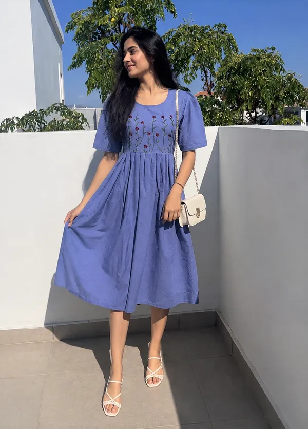 This_is_a_blue_knee-length_A-line_dress_with_short_sleeves_and_a_round_neckline._The_bodice_features_colorful_floral_embroidery._It_is_paired_with_a_beige_shoulder_bag_and_beige_sandals._This_style_is_suitable_for_casual_outings,_brunches,_or_daytime_events.