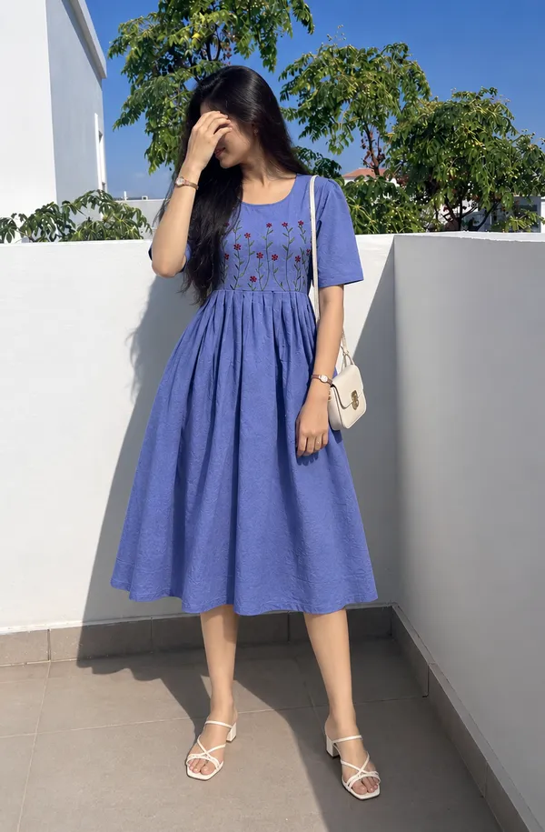 This_is_a_blue_knee-length_A-line_dress_with_short_sleeves_and_a_round_neckline._The_bodice_features_colorful_floral_embroidery._It_is_paired_with_a_beige_shoulder_bag_and_beige_sandals._This_style_is_suitable_for_casual_outings,_brunches,_or_daytime_events.