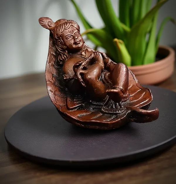 Brownish-Orange_Copper_Idols,_6_Cm,_Handmade_Bal_Krishna_Lying_In_Banyan_Leaf_82_Gram,_Patina_Antique_Finish,_Pack_Of_1_Piece